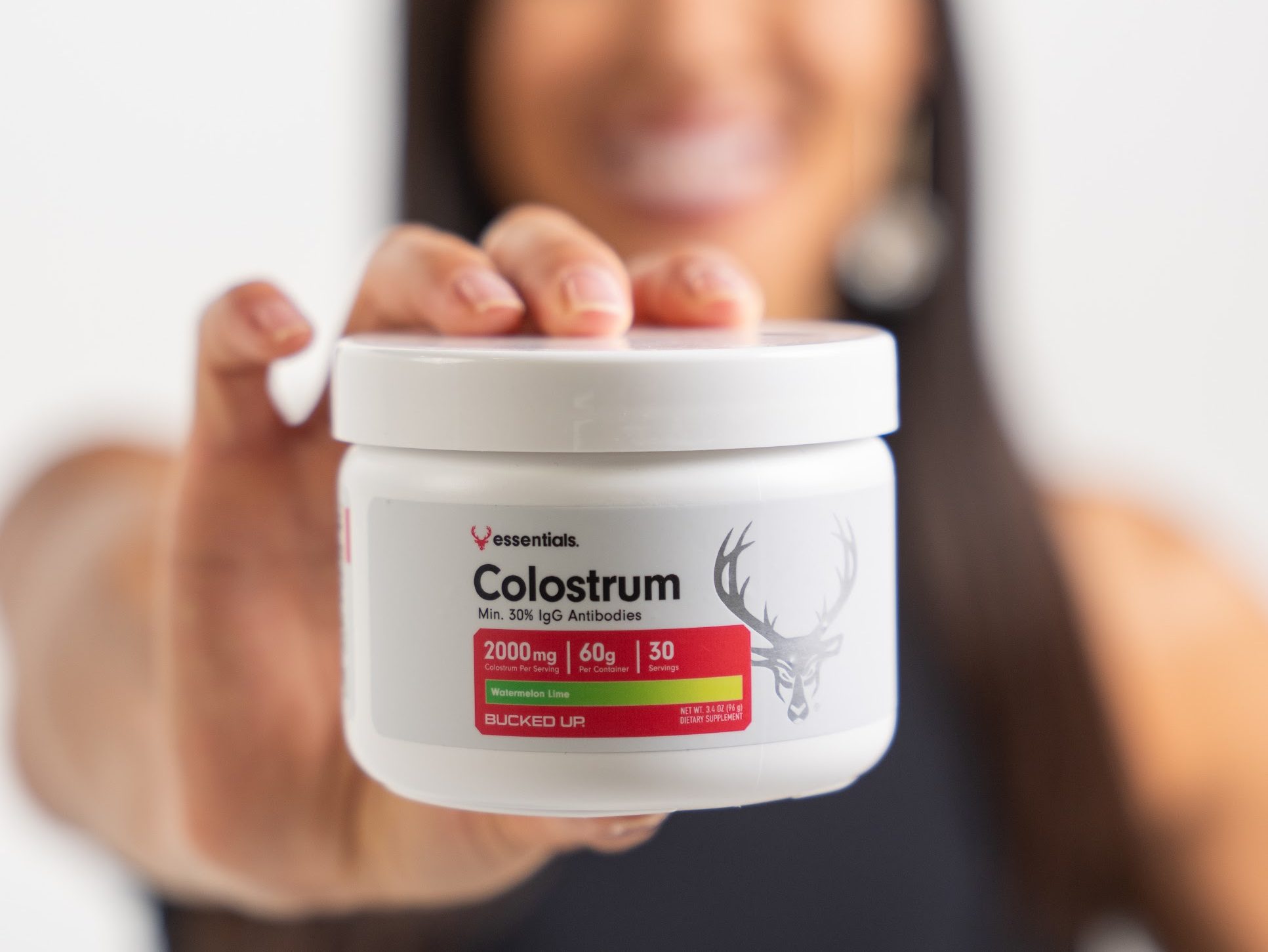 Image of a woman holding Bucked Up Colostrum in front of her (watermelon lime flavor).